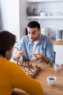 Genç İspanyol adam babasıyla mutfakta satranç oynarken parmağını göstererek ön planı bulanıklaştırdı.
