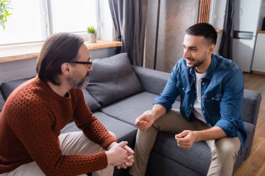 Genç İspanyol adam evde kanepede babamla konuşurken el hareketi yapıyor.