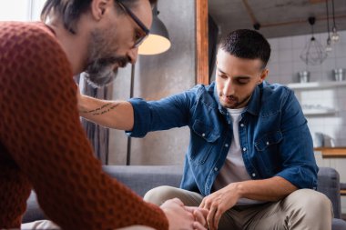 Genç İspanyol adam evde üzgün babasını sakinleştiriyor, ön planda bulanıklık var.