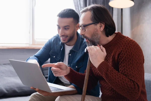 Ámulatba Esett Férfi Sétapálcával Mutatva Laptop Közelében Fiatal Spanyol Fiú — Stock Fotó