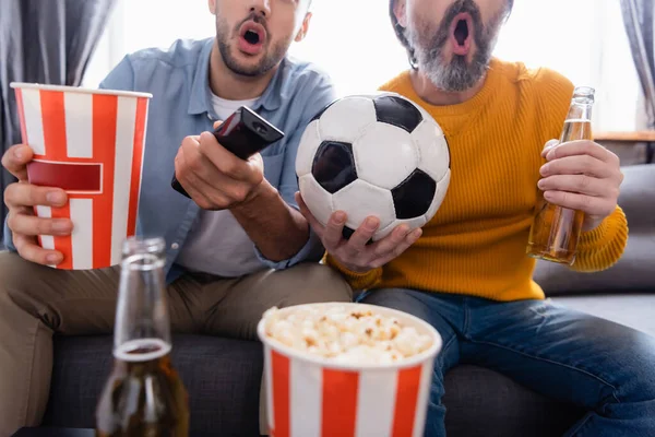 partial view of excited father and son watching football match on tv at home, blurred background