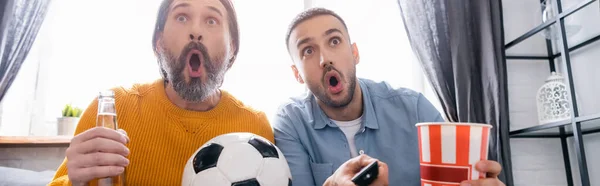 excited interracial father and son watching football championship at home, banner