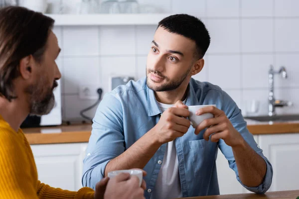 Young Hispanic Man Holding Coffee Cup While Listening Father Conversation — Stock Photo, Image