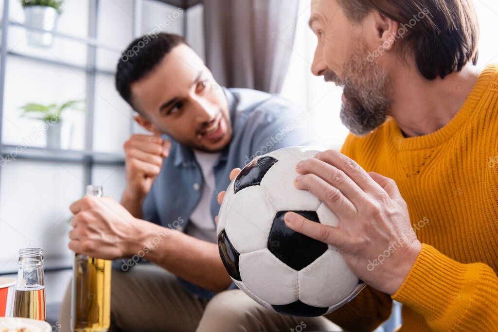 young hispanic man showing win gesture while watching football match with dad at home, blurred background