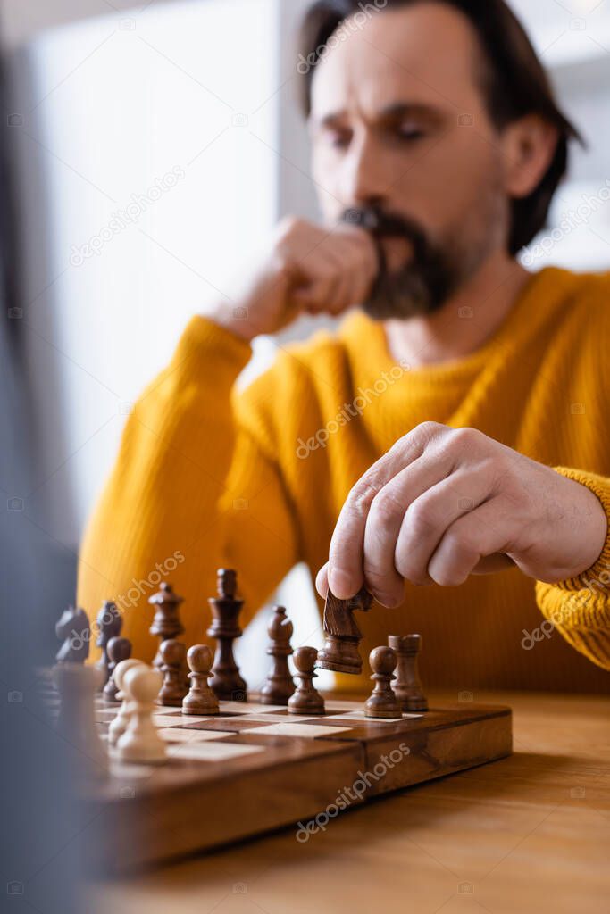 selective focus of thoughtful man playing chess on blurred foreground