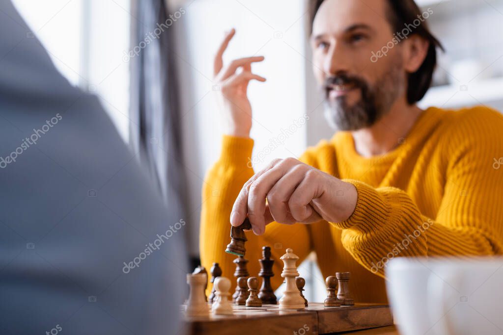 selective focus of bearded man gesturing while playing chess on blurred foreground