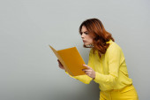 shocked woman in yellow blouse staring at notebook on grey