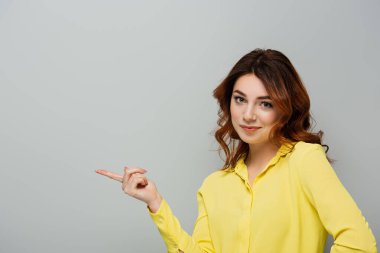 smirking woman looking at camera while pointing with finger on grey clipart