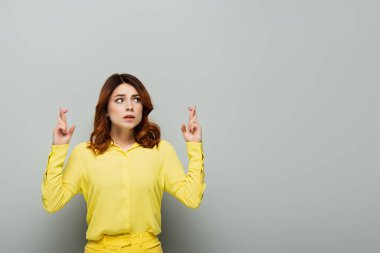 worried woman standing with crossed fingers and looking away on grey clipart