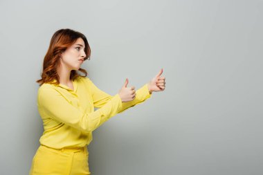 jealous woman looking away and showing thumbs up on grey clipart