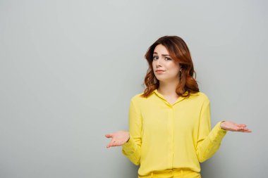 Gri renkli kameraya bakarken omuz silkme hareketi yapan hoşnutsuz bir kadın.