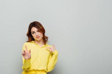haughty woman pointing with finger at herself while showing stop gesture on grey