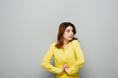 Korkmuş bir kadın, elleri griye kenetlenmiş vaziyette dikilirken gözlerini kaçırıyor.
