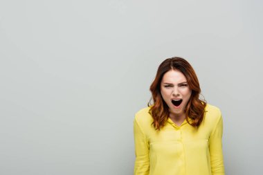 angry woman in yellow blouse screaming while looking at camera on grey clipart