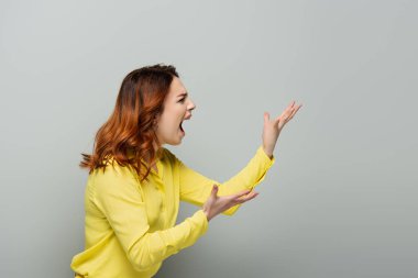 irritated woman in yellow shirt shouting while pointing with hands on grey clipart