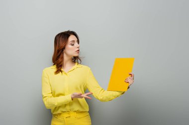 arrogant woman in yellow blouse pointing at notebook on grey clipart