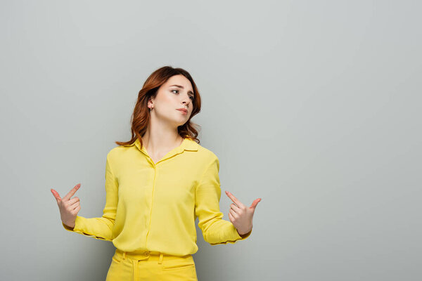 arrogant woman pointing with fingers at herself while looking away on grey