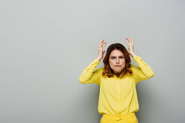 недовольная женщина с руками возле головы, смотрящая в камеру на сером