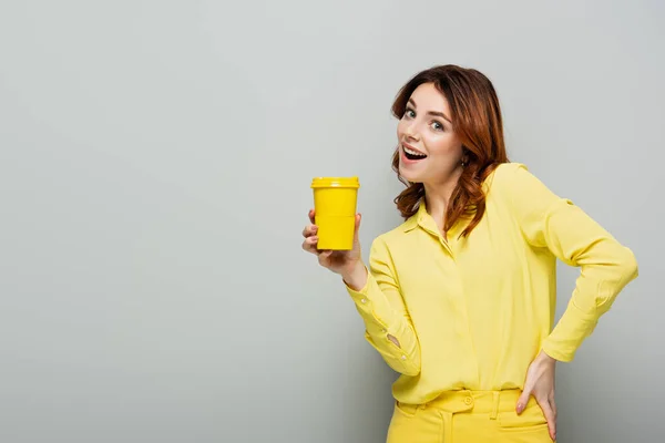 Весела Жінка Тримає Жовту Паперову Чашку Стоячи Рукою Стегні Сірому — стокове фото