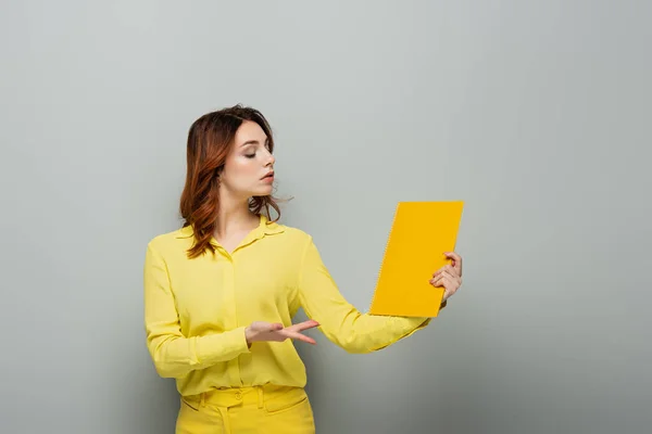 arrogant woman in yellow blouse pointing at notebook on grey