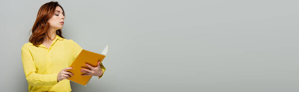 haughty woman in yellow shirt looking at notepad on grey, banner