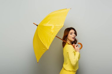 Sarı şemsiyeyle gri üzerine poz verirken dilinden dışarı fırlayan çiftçi kadın.