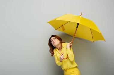 Gri üzerinde sarı şemsiye tutan hoşnutsuz bir kadın.