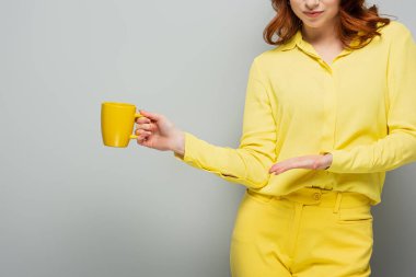 Kırpılmış sarı elbiseli kadın gri bardağı işaret ediyor.