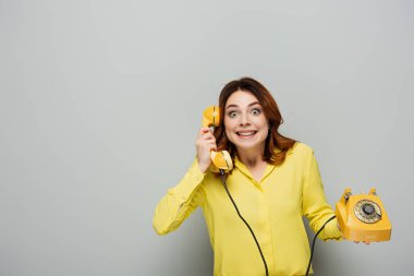 Gri üzerinde retro telefonda konuşurken kameraya bakan heyecanlı kadın