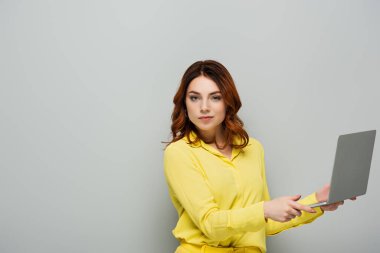 Gri dizüstü bilgisayarla kameraya bakan emin bir kadın.