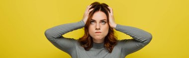irritated woman looking up while touching head isolated on yellow, banner clipart