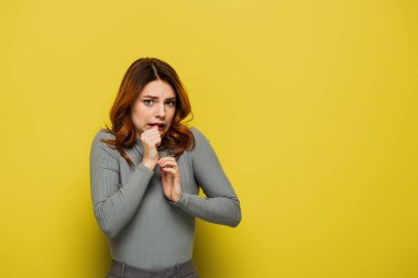 anxious woman looking at camera while holdings hands near face on yellow clipart