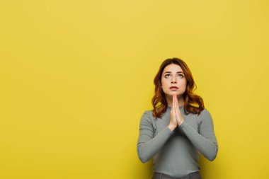 tense woman showing please gesture while looking up on yellow clipart