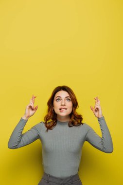 hopeful woman holding crossed fingers while looking up on yellow clipart