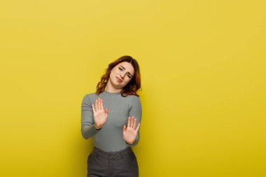 dissatisfied woman looking at camera while showing stop gesture on yellow clipart