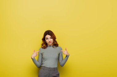 Kırgın, kıvırcık saçlı, sarı saçlı bir kadın kendini işaret ediyor.