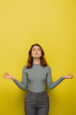 Kıvırcık saçlı ve gözleri kapalı bir kadın, sarıda meditasyon yaparken yanaklarını şişiriyor
