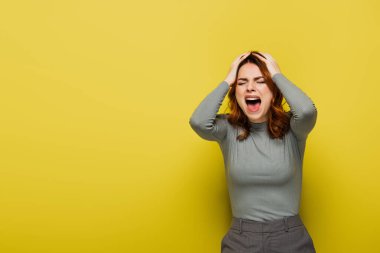 angry woman with wavy hair screaming and touching head on yellow  clipart