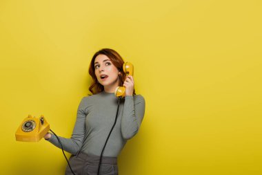 Sarı renkte retro telefonu tutan genç bir kadın.