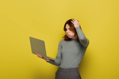 Şok olmuş kıvırcık saçlı yanaklı bir kadın dizüstü bilgisayarını sarıda tutarken