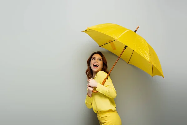 Excited Woman Looking Away While Standing Yellow Umbrella Grey — Stock Photo, Image