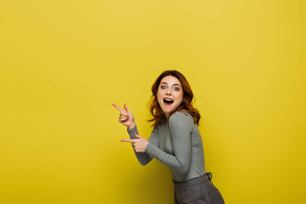 astonished woman pointing with fingers while looking at camera on yellow