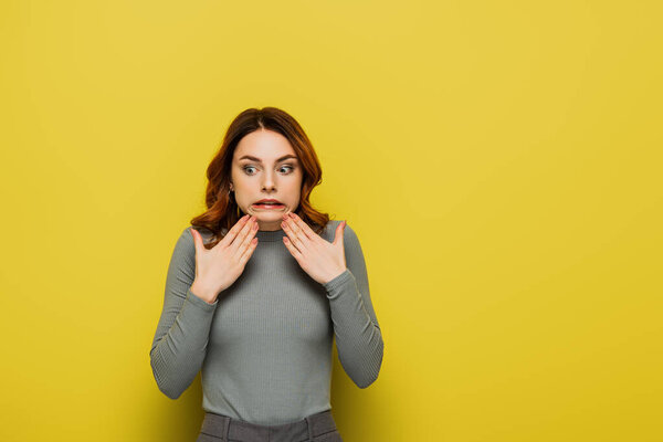 affected woman grimacing while holding hands near chin on yellow