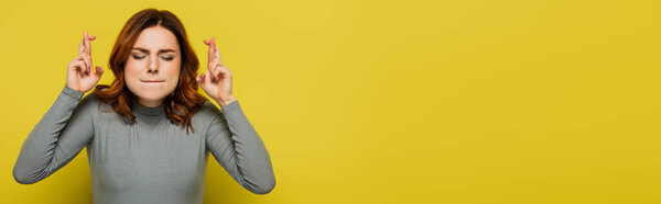 tense woman with crossed fingers standing with closed eyes on yellow, banner