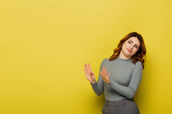 disgusted woman showing stop gesture while looking away on yellow