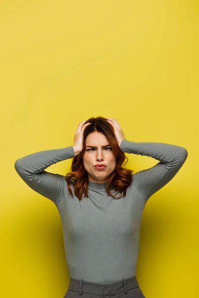 stressed woman touching head while suffering from headache on yellow