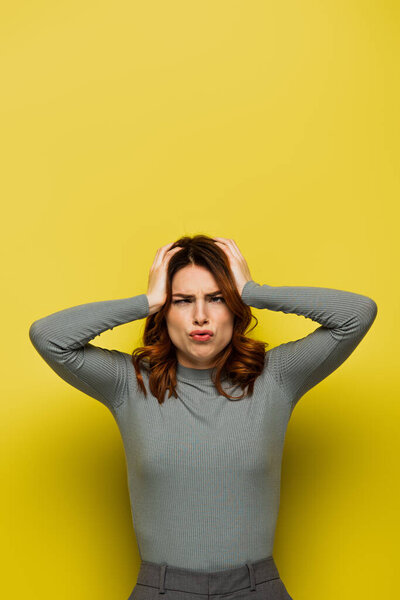 stressed woman touching head while suffering from headache on yellow