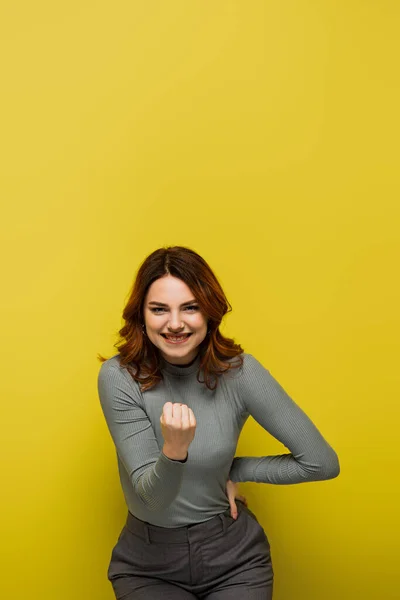 Кучерява Жінка Згорнутим Кулаком Рукою Стегні Стоячи Посміхаючись Жовтому — стокове фото