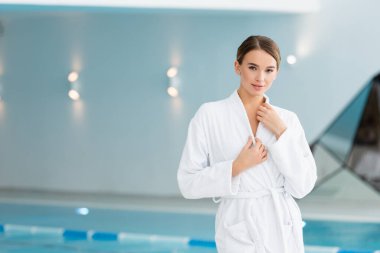 Güzel genç bir kadın spa merkezinde bornozu ayarlıyor. 