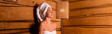 Pleased woman in towels sitting in sauna, banner  clipart